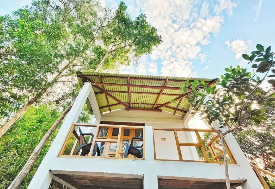 An elevated white cottage with a corrugated awning roof at Dolubari Eco Resort, seen from below against the sky